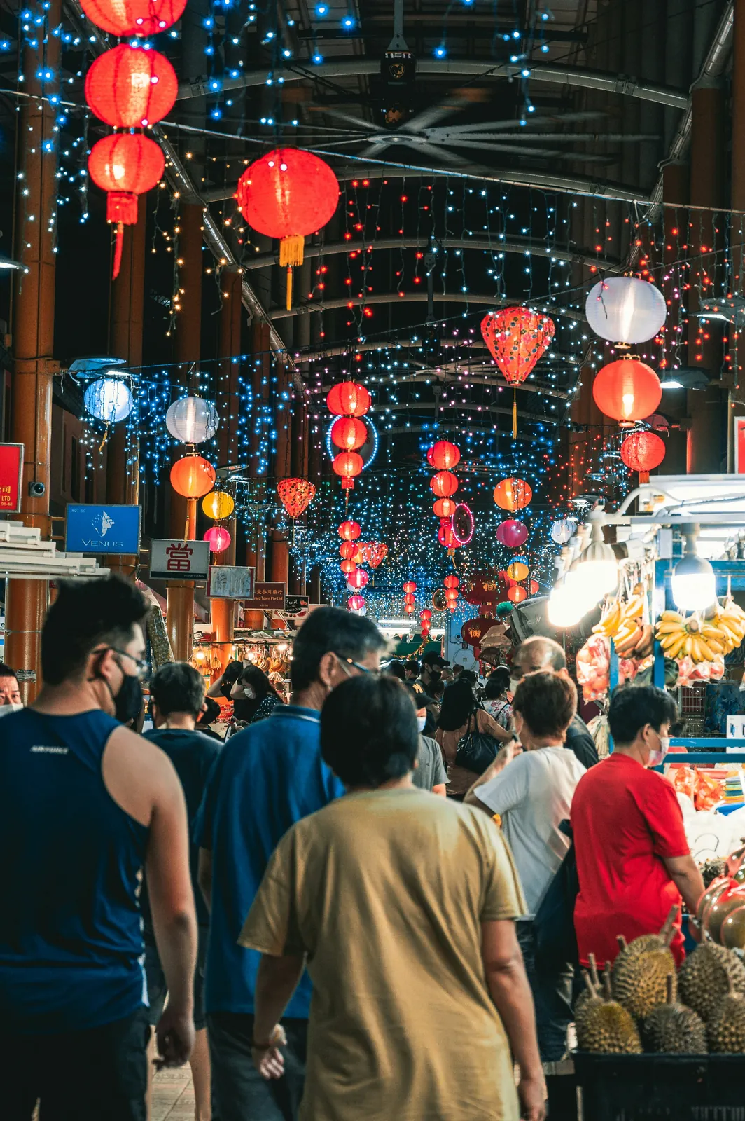 A busy covered market lane hung with red lanterns in the evening