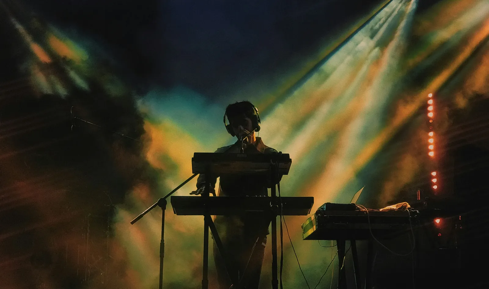 A musician playing keyboards on stage under coloured lights