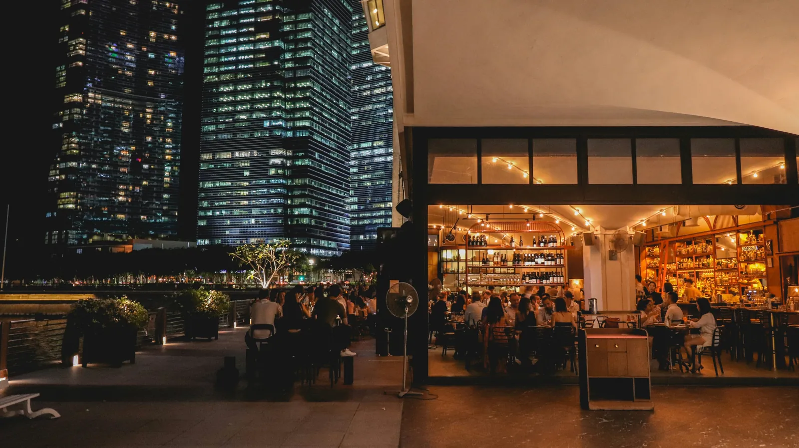 People at a waterfront wine bar in the evening with the city skyline behind